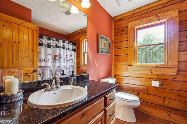 bathroom featuring visible vents, wood walls, toilet, vanity, and a textured ceiling