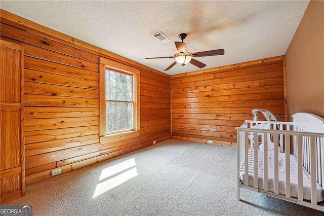 unfurnished bedroom with visible vents, carpet floors, a textured ceiling, and wooden walls