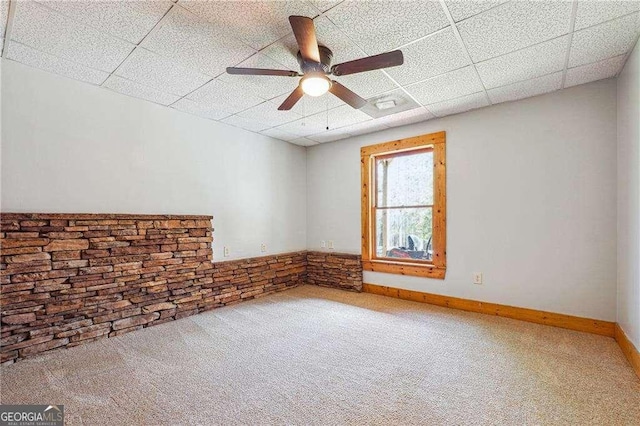 carpeted empty room with a drop ceiling, baseboards, and ceiling fan