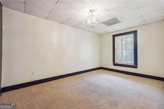 carpeted empty room featuring a notable chandelier, a drop ceiling, and baseboards