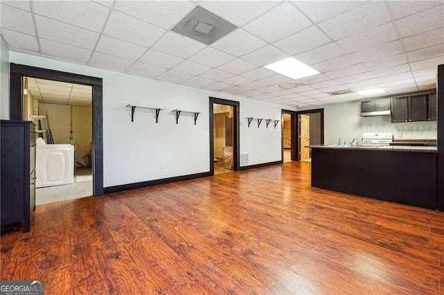 kitchen with baseboards, a drop ceiling, washing machine and dryer, wood finished floors, and white electric stove