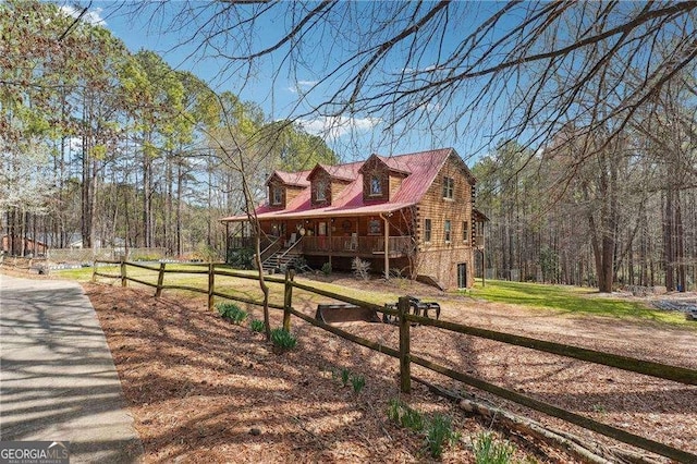 view of front of home featuring a front yard, fence, a wooded view, a porch, and log siding