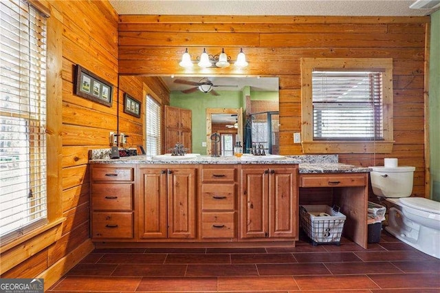 bathroom featuring toilet, a stall shower, wood walls, and a sink