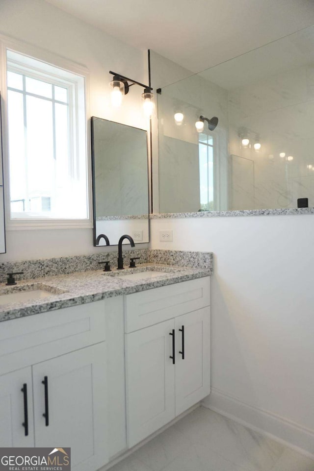 bathroom with double vanity, marble finish floor, a walk in shower, and a sink