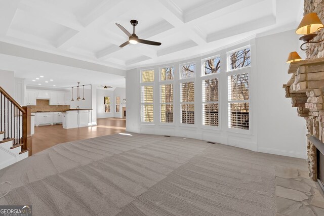 unfurnished living room featuring beam ceiling, a ceiling fan, coffered ceiling, a fireplace, and stairs