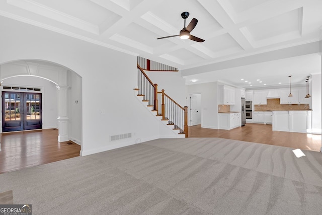 unfurnished living room featuring visible vents, a high ceiling, arched walkways, stairs, and light carpet