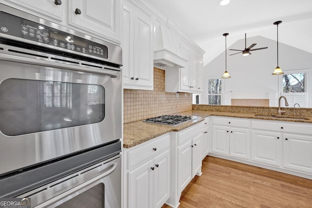 kitchen with a sink, white cabinetry, stainless steel appliances, light wood finished floors, and lofted ceiling