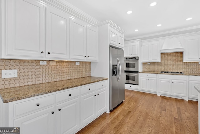 kitchen with light stone counters, stainless steel appliances, white cabinets, light wood-style floors, and backsplash