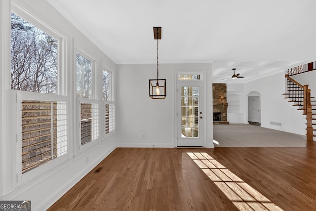 unfurnished dining area featuring visible vents, a fireplace, stairs, and wood finished floors