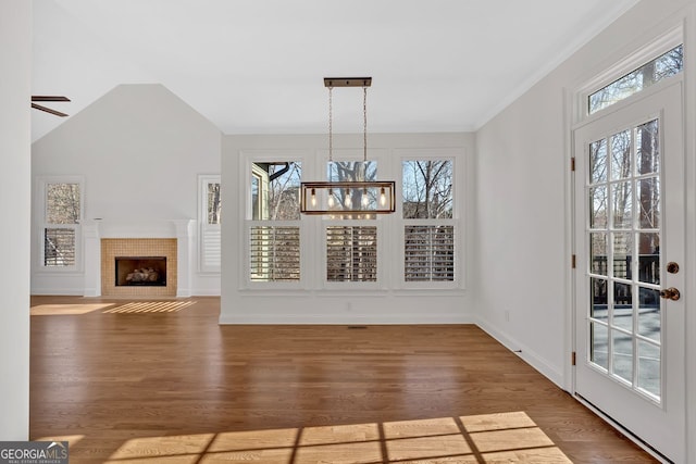 unfurnished dining area featuring a fireplace with flush hearth, a notable chandelier, lofted ceiling, wood finished floors, and baseboards