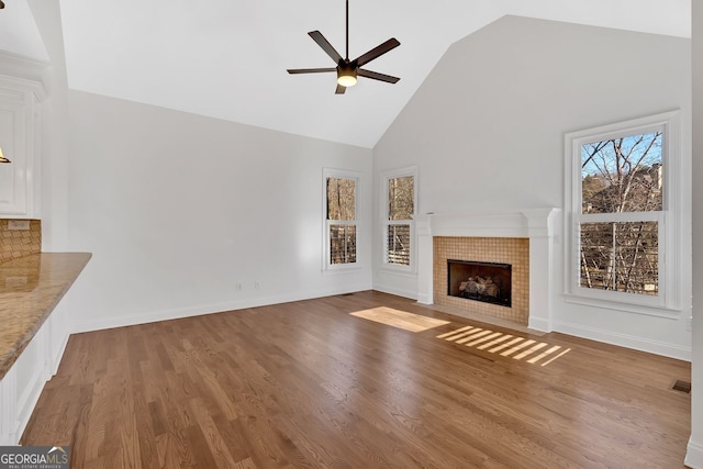 unfurnished living room with visible vents, a ceiling fan, wood finished floors, and a tiled fireplace