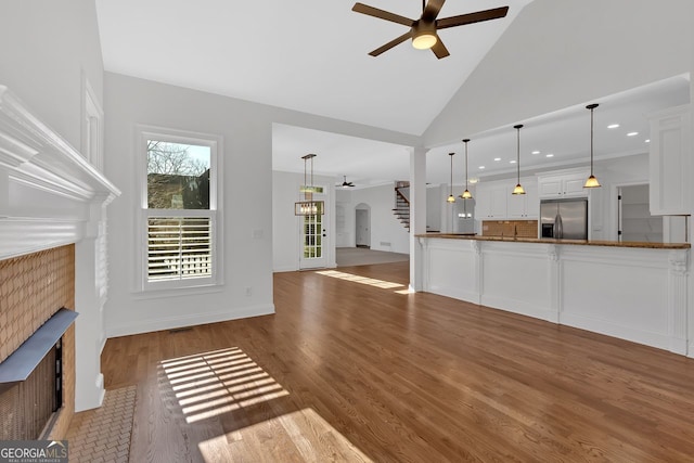 unfurnished living room with high vaulted ceiling, wood finished floors, stairway, a fireplace, and ceiling fan