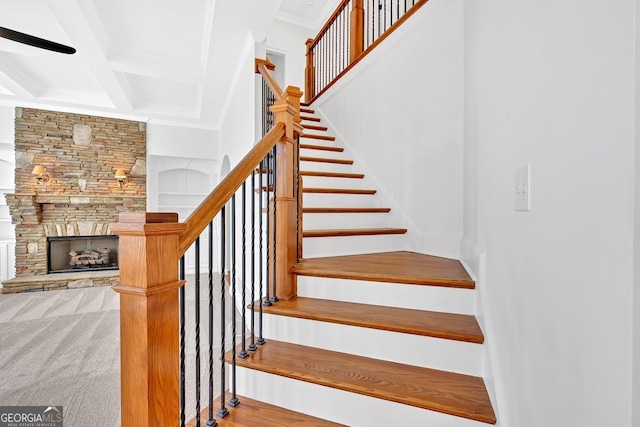 staircase with crown molding, beam ceiling, a stone fireplace, a high ceiling, and coffered ceiling