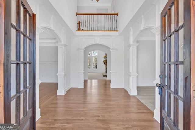 foyer entrance featuring decorative columns, arched walkways, light wood-style floors, and a towering ceiling