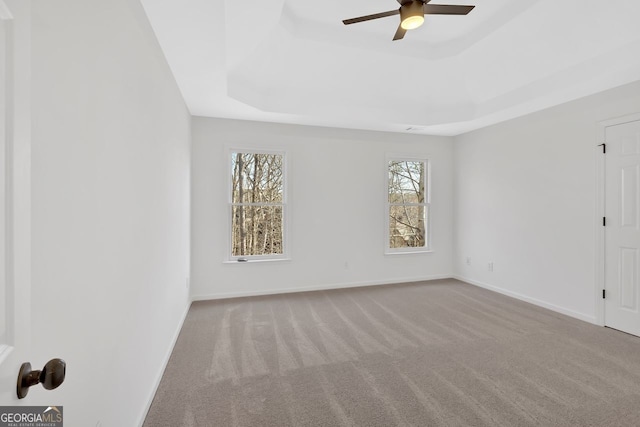 unfurnished room featuring a tray ceiling, carpet floors, baseboards, and a ceiling fan