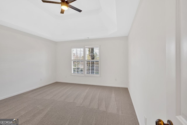 carpeted spare room with baseboards, a raised ceiling, and ceiling fan