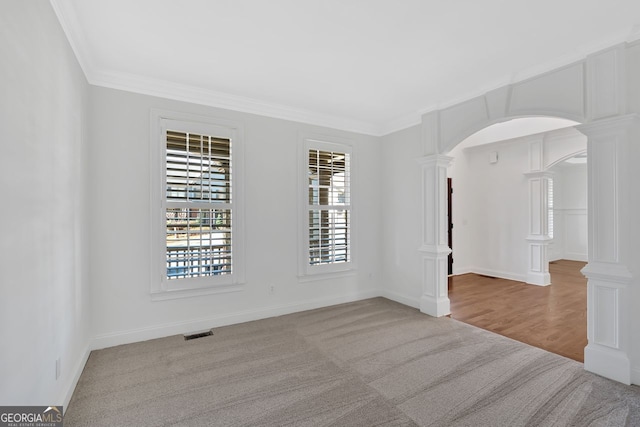 spare room featuring visible vents, decorative columns, arched walkways, crown molding, and carpet flooring