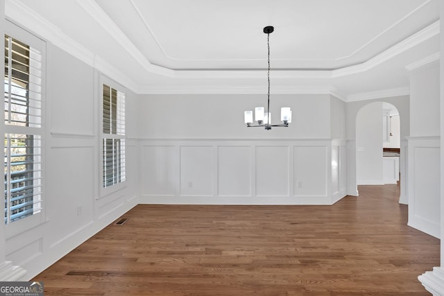 unfurnished dining area with arched walkways, a chandelier, a tray ceiling, and wood finished floors