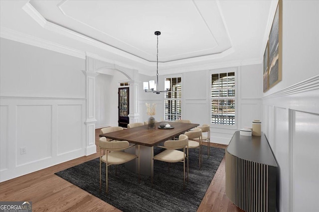 dining room with ornate columns, a tray ceiling, arched walkways, and a decorative wall