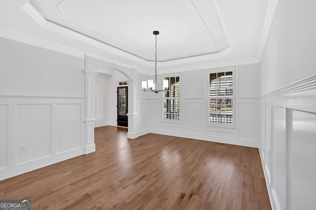 unfurnished dining area featuring a tray ceiling, arched walkways, wood finished floors, and decorative columns