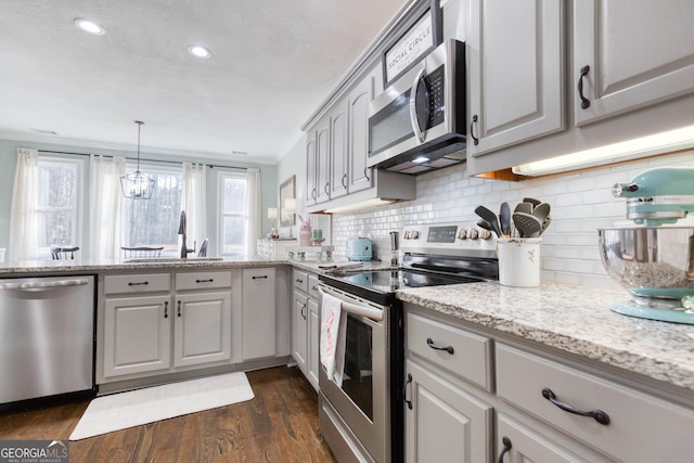 kitchen with a sink, light stone counters, dark wood finished floors, appliances with stainless steel finishes, and decorative backsplash