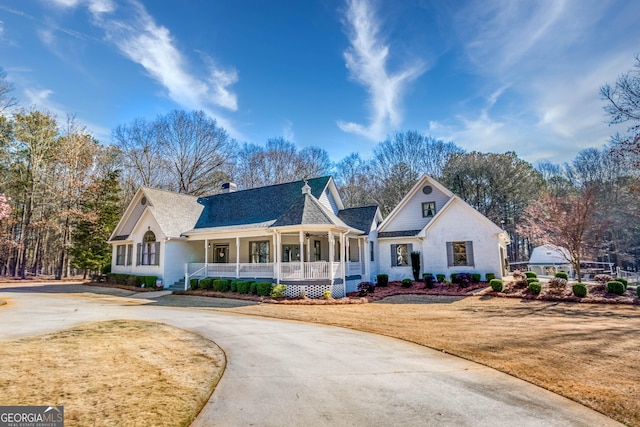 view of front of house featuring a shingled roof, concrete driveway, a front yard, covered porch, and a chimney