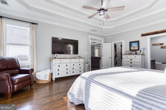 bedroom featuring wood finished floors, visible vents, a tray ceiling, ornamental molding, and a barn door