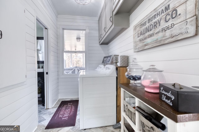 clothes washing area with cabinet space, crown molding, wooden walls, and washing machine and dryer