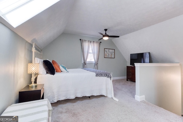 carpeted bedroom with vaulted ceiling with skylight and a ceiling fan