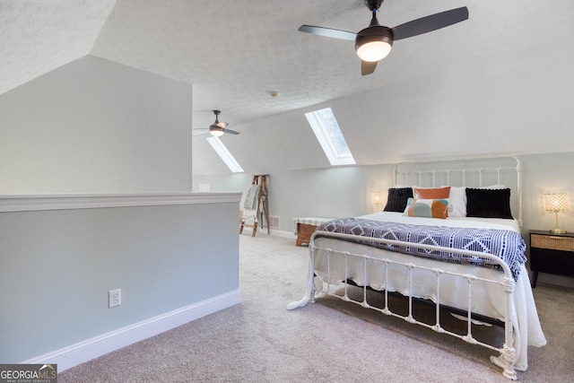 carpeted bedroom featuring ceiling fan, vaulted ceiling with skylight, baseboards, and a textured ceiling