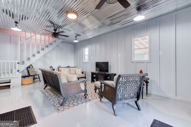 living area featuring a decorative wall, stairs, concrete flooring, and a ceiling fan