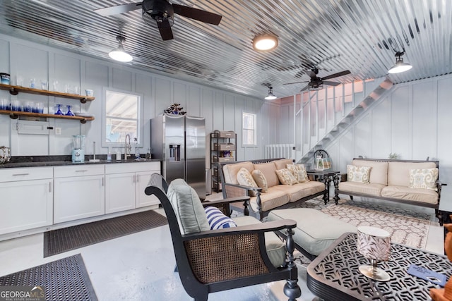 living area featuring stairway, a ceiling fan, and a decorative wall