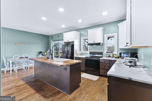 kitchen with black appliances, light wood-style floors, under cabinet range hood, wood counters, and white cabinetry