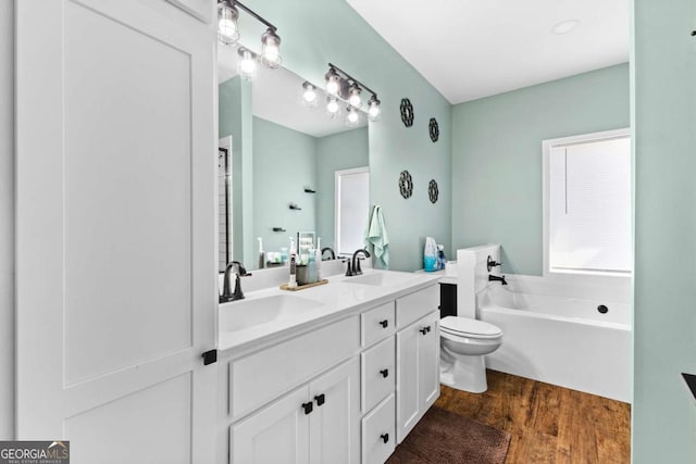 bathroom with a garden tub, wood finished floors, double vanity, and a sink