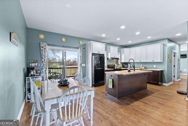 kitchen with an island with sink, light wood-style flooring, white cabinetry, and electric stove