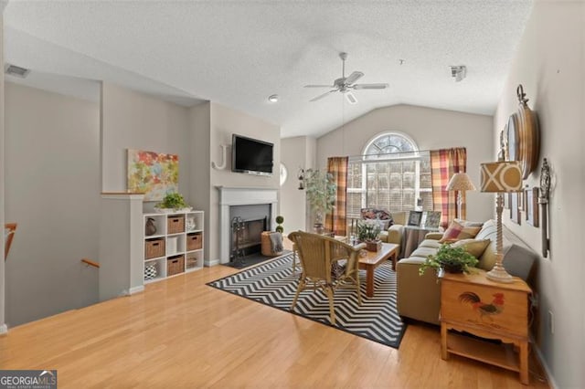 living room with a fireplace with flush hearth, a ceiling fan, a textured ceiling, wood finished floors, and lofted ceiling