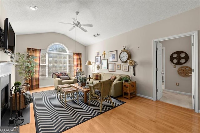 living room featuring lofted ceiling, a fireplace, ceiling fan, a textured ceiling, and light wood-type flooring