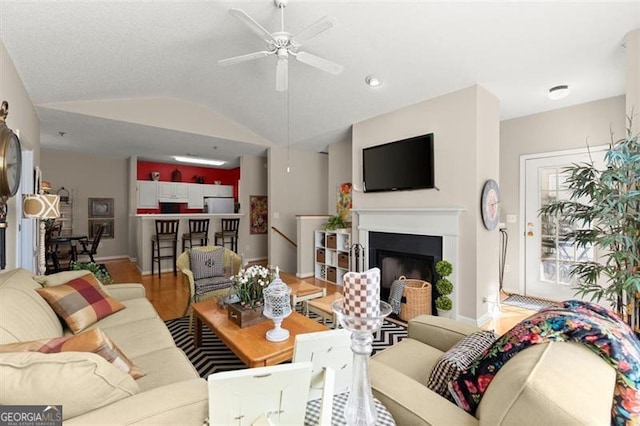 living room with a ceiling fan, wood finished floors, a fireplace, baseboards, and vaulted ceiling