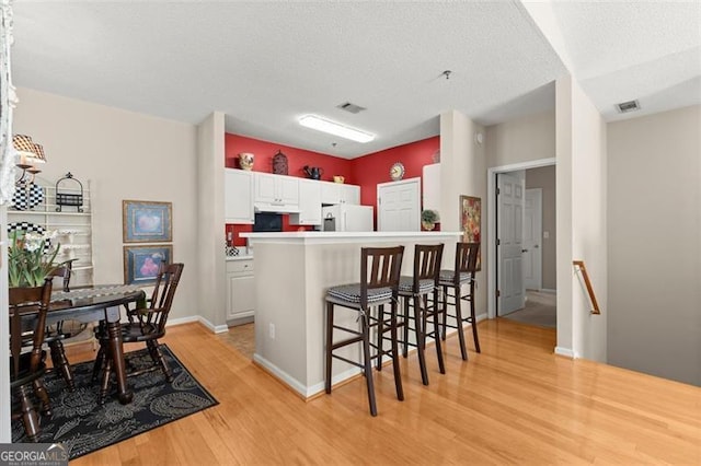 kitchen with a breakfast bar, a peninsula, light wood-style floors, white fridge with ice dispenser, and white cabinets