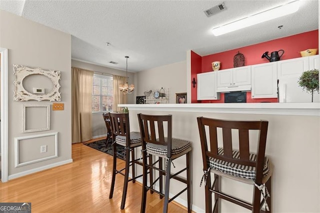 kitchen featuring visible vents, white cabinets, under cabinet range hood, a kitchen bar, and light wood-type flooring