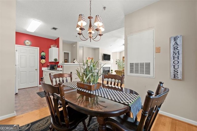 dining space with visible vents, baseboards, light wood-style flooring, a fireplace, and a textured ceiling