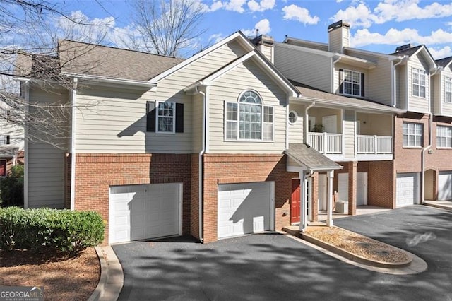 view of front facade with brick siding, driveway, an attached garage, and a chimney