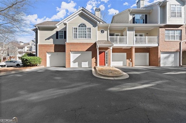 multi unit property featuring a garage, brick siding, driveway, and a chimney