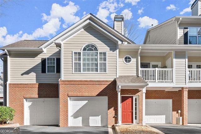 townhome / multi-family property featuring a balcony, driveway, a chimney, a garage, and brick siding