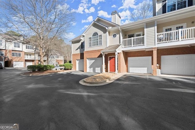 view of front of home featuring a garage, brick siding, driveway, and a chimney