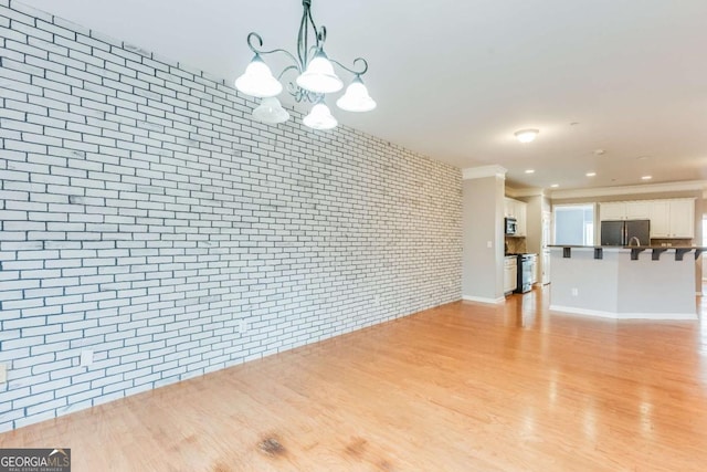 unfurnished living room featuring light wood-style floors, baseboards, brick wall, and a chandelier