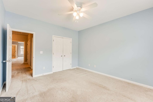 unfurnished bedroom featuring baseboards, attic access, ceiling fan, a closet, and light colored carpet