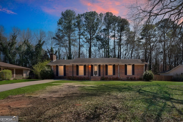 ranch-style house featuring a front yard, brick siding, concrete driveway, and a chimney