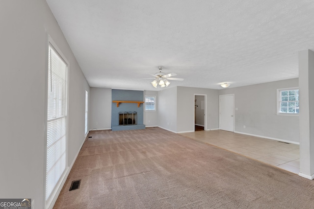 unfurnished living room featuring visible vents, a textured ceiling, a fireplace, carpet flooring, and a healthy amount of sunlight