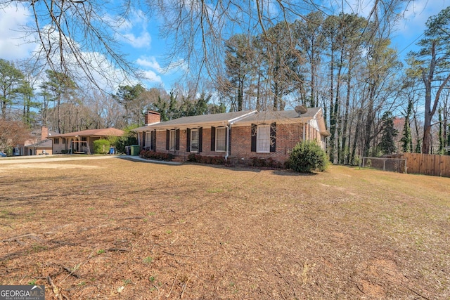 ranch-style home featuring brick siding, a chimney, a front yard, and fence